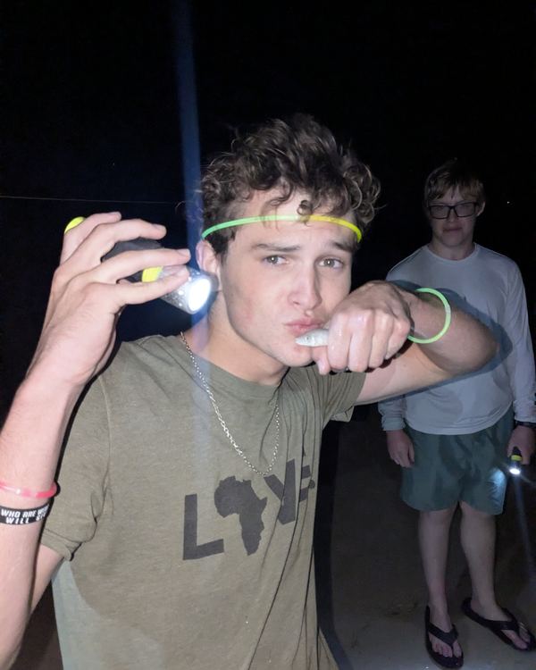 A guest in a glow headband holding a flashlight on the beach at night