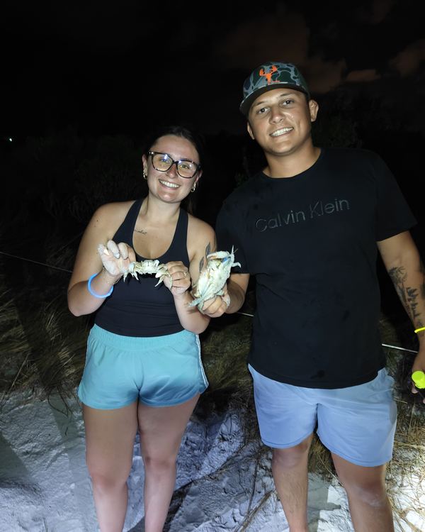 A smiling couple on the beach at night, both holding up the crabs they caught